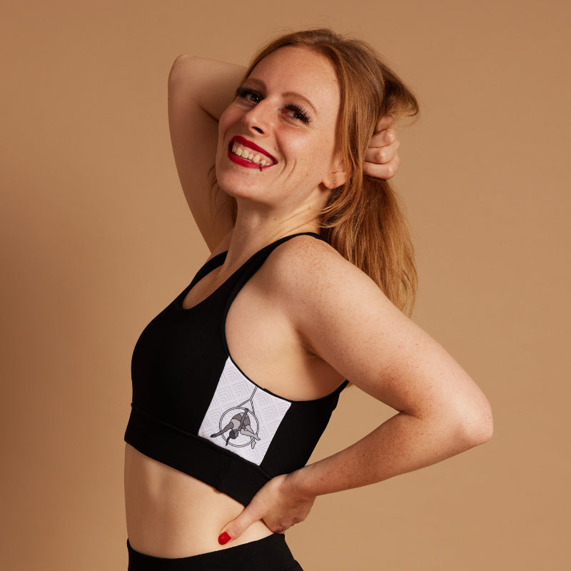 female shown from the toros up, smiling with one hand in her hair, showing off the print panel on the Signature Aerial bra she's wearing